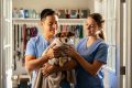 Volunteer gently holding a rescued dog in a foster home doorway with another volunteer preparing comfort care nearby.